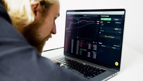 Über-die-Schulter-Ansicht eines Mannes am Laptop mit Krypto-Trading-Dashboard